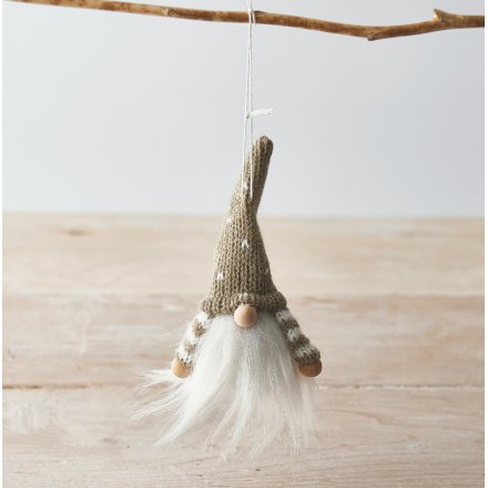 Knitted gnome ornament hanging on a branch with a light background