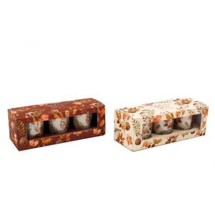 Two sets of small candles in decorative boxes with autumn-themed designs on a white background.