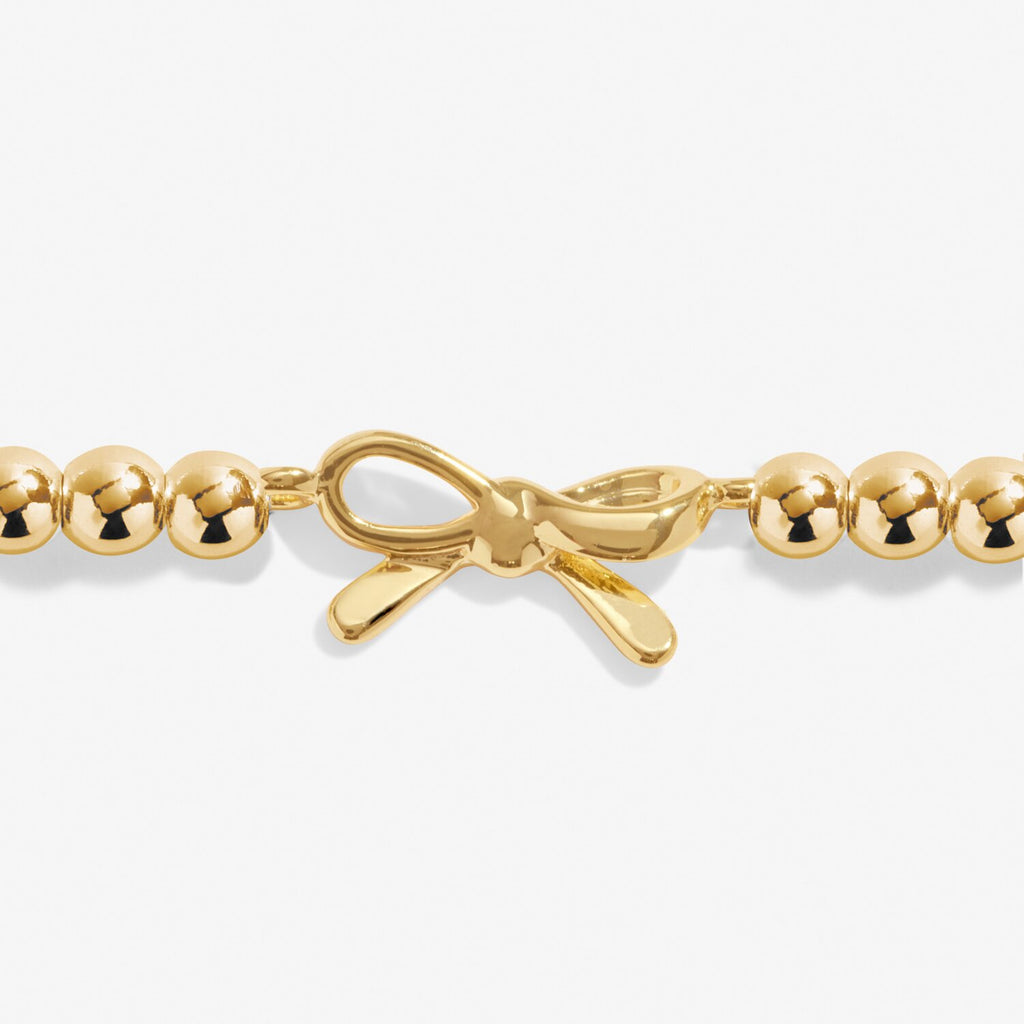 Gold bracelet with a bow charm on a white background