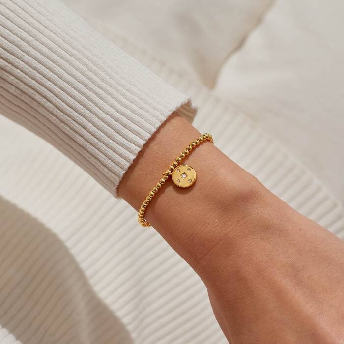 Gold bracelet on a wrist with a neutral background