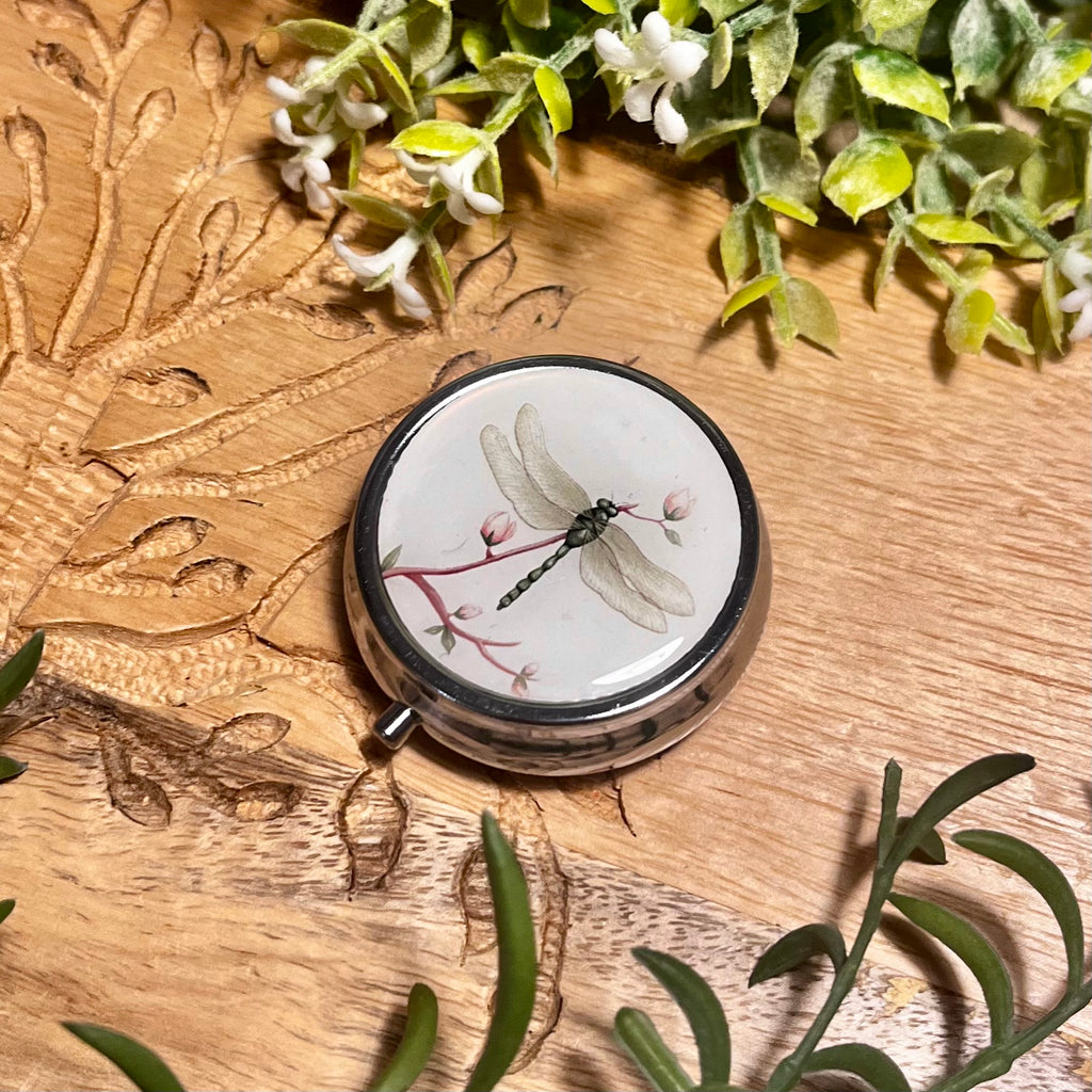 round silver pill box with cream top and a dragonfly on 
