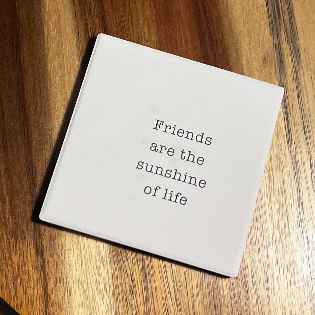 Square white coaster with the quote 'Friends are the sunshine of life' in typewriter font