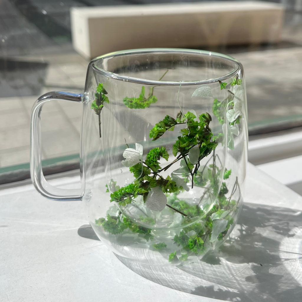 Transparent glass mug with white flowers sitting inside the double walls of glass. 