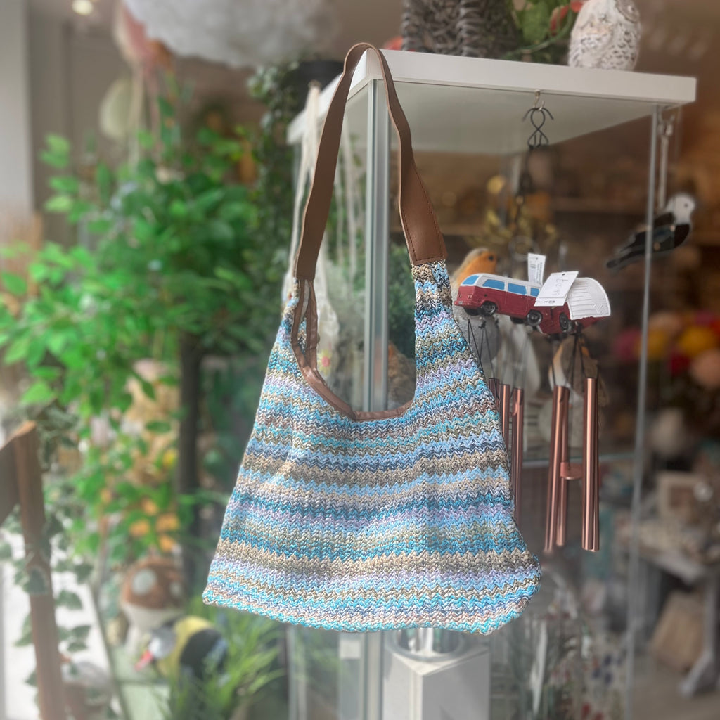 Shoulder bag with brown leather strap and a woven style body. Sporadically alternates colours of muted blues and greens. 
