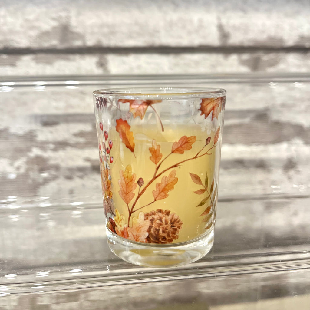 Glass candle holder with autumn leaf design on a reflective surface