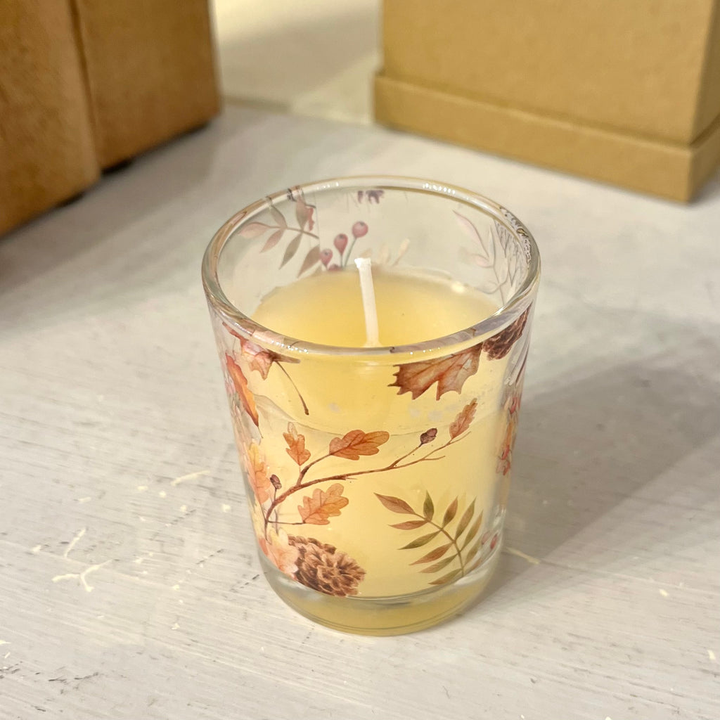 Individual candle in glass jar with autumnal leaf design on a wooden background