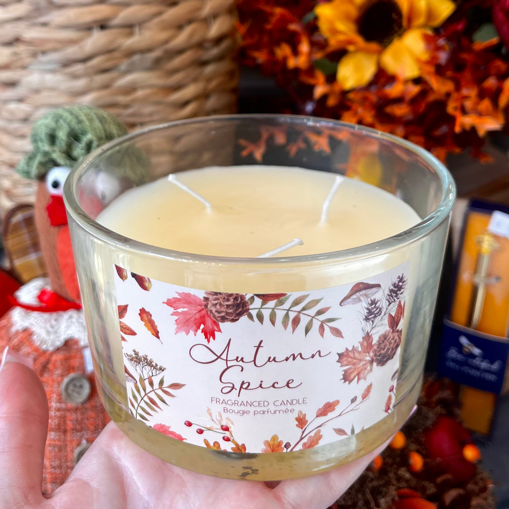 Hand holding a 'Autumn Spice' scented candle with decorative elements in the background.