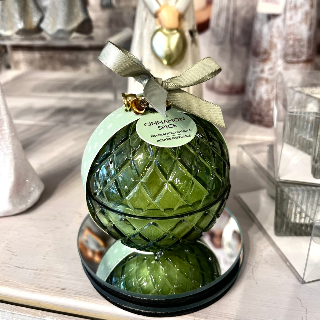 Green glass ornament with a ribbon on a reflective surface