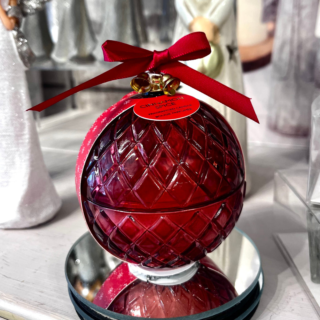Red glass ornament with a red ribbon and tag on a reflective surface