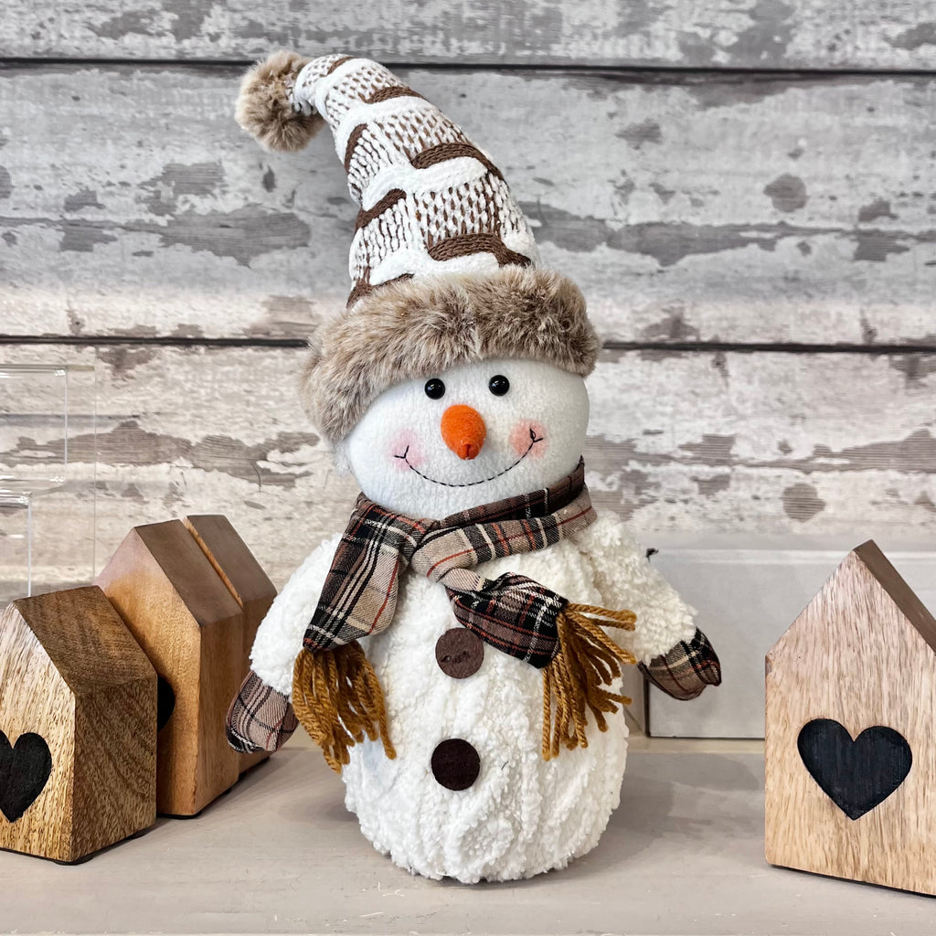 Decorative snowman with a plaid scarf, hat, and carrot nose on a wooden background.