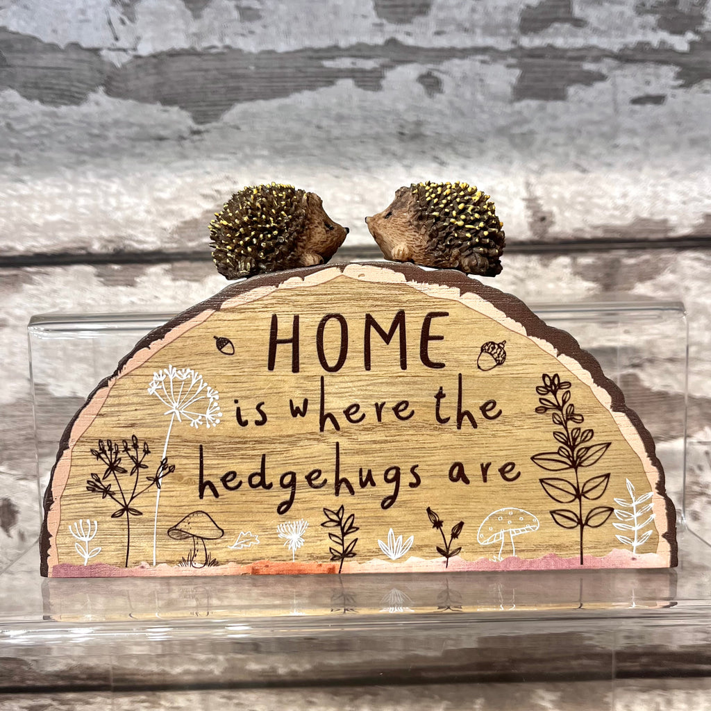Wooden sign with 'HOME is where the hedgehugs are' text and hedgehog figures on a wooden background.
