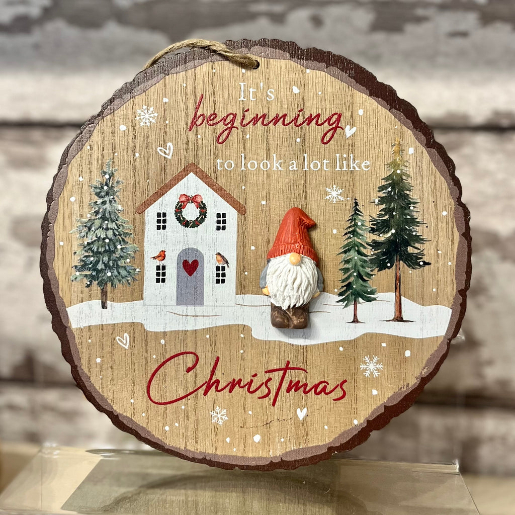 Decorative wooden ornament with a house, gnome, and trees on a snowy background.