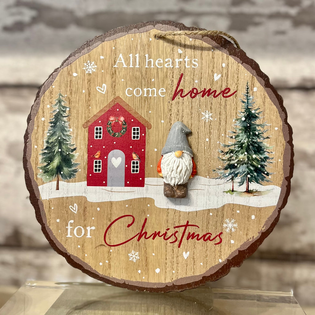 Decorative wooden ornament with a red house, gnome, and Christmas trees on a wooden background.
