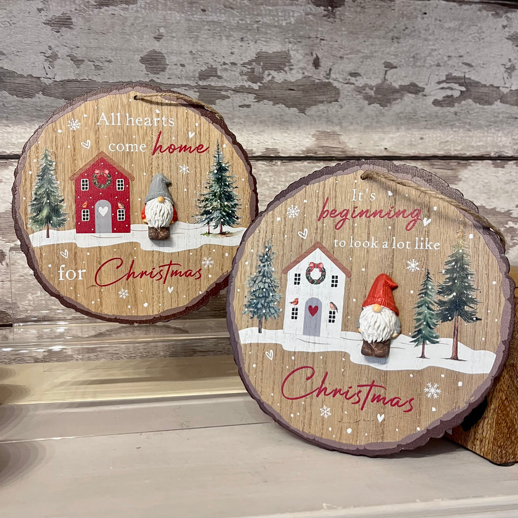 Two wooden Christmas decorations with festive scenes and text on a wooden surface.