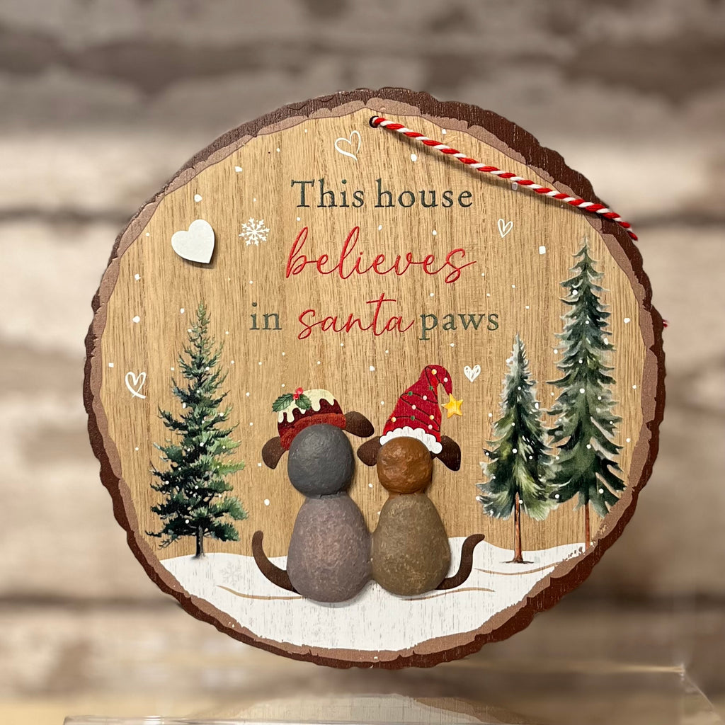 Decorative wooden sign with two dogs wearing Santa hats and text 'This house believes in santa paws' on a wooden background.