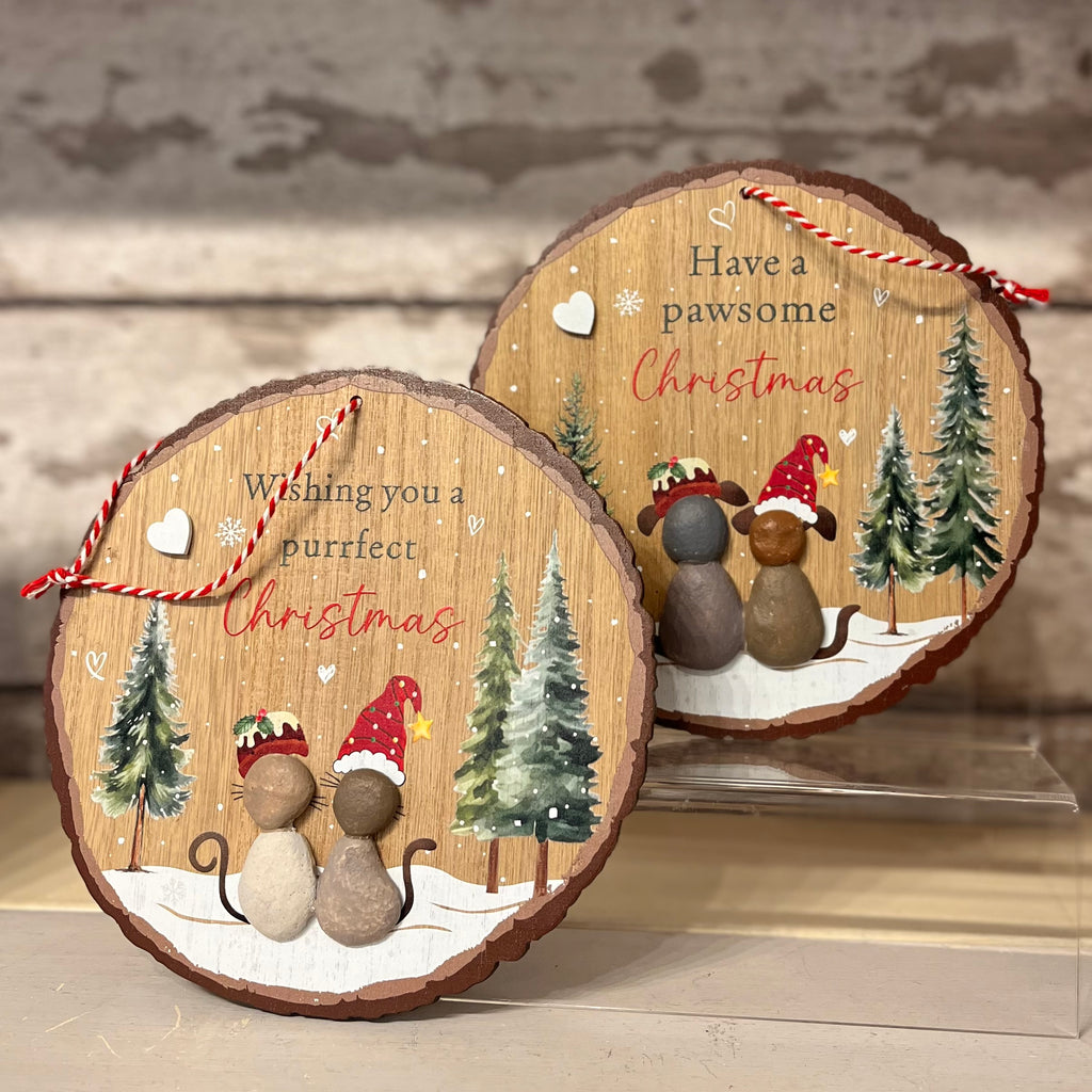 Two wooden Christmas ornaments with festive designs and text on a neutral background.