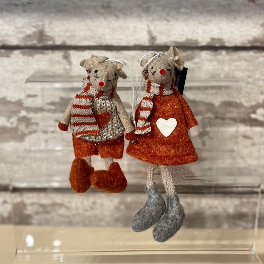 Two stuffed animal figures, one in a coat with a heart design and the other in a sweater and shorts, on a reflective surface.