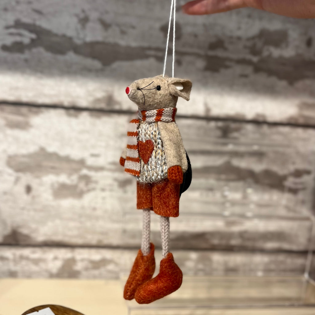 Handmade toy mouse in a sweater with heart pattern, hanging against a wooden background.