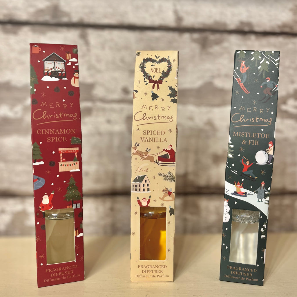 Three Christmas-themed diffuser boxes on a wooden surface with a blurred background.