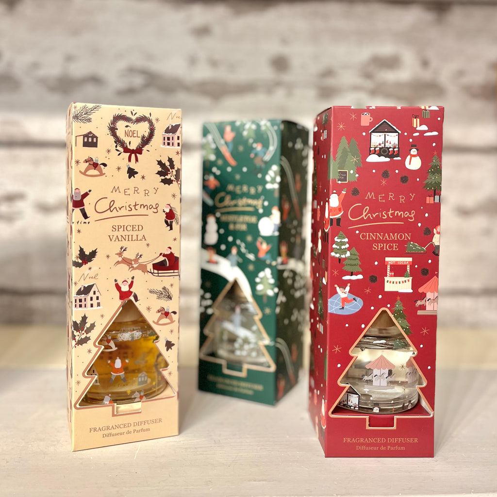 Three Christmas-themed diffuser boxes with festive designs on a neutral background