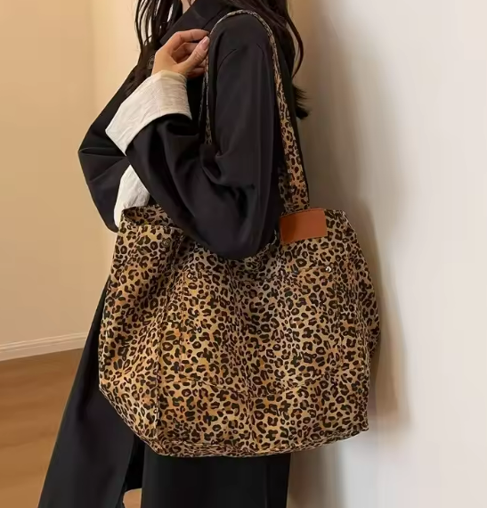 Brown leopard print tote bag with shoulder straps and leather patch underneath one shoulder strap.