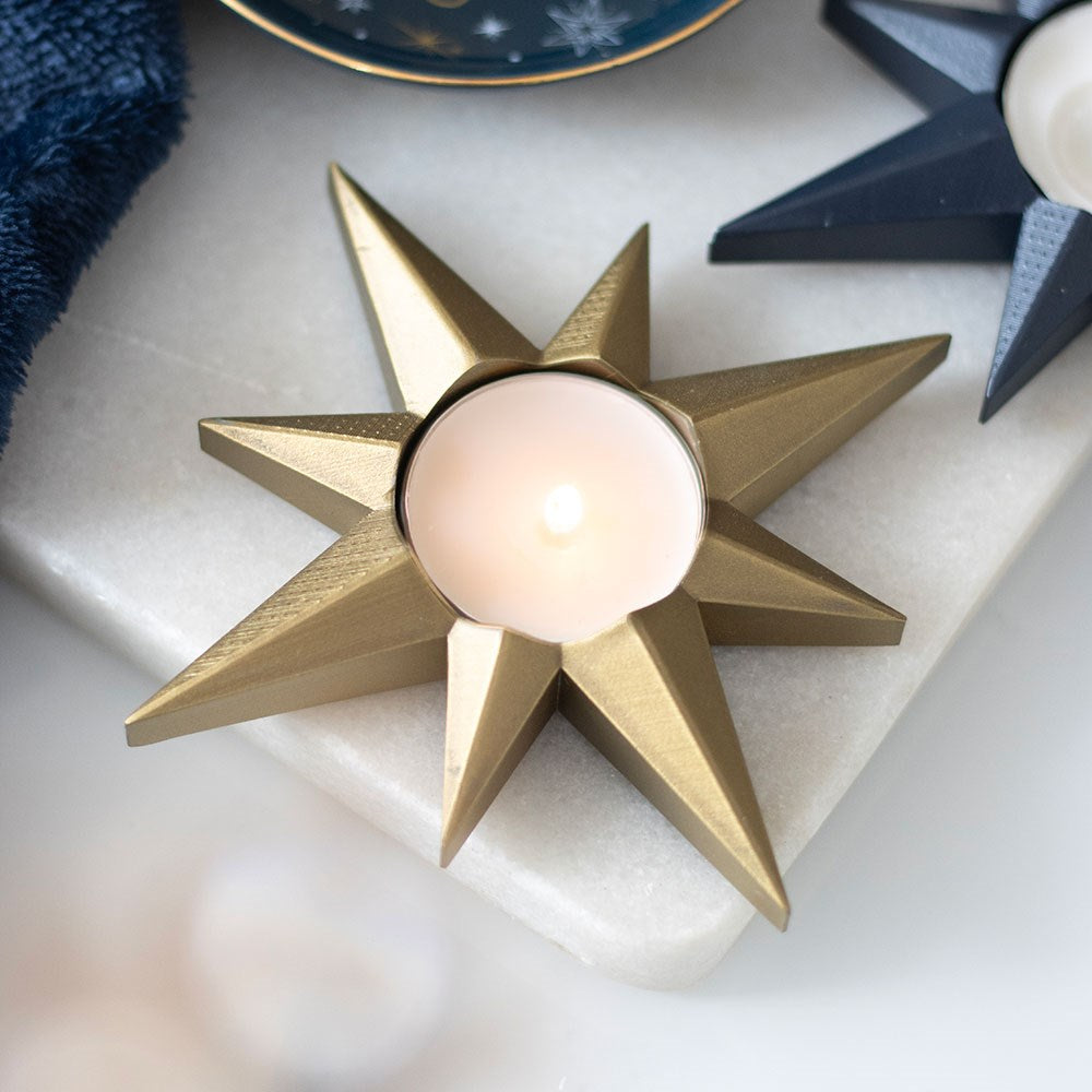Gold star-shaped candle holder with a lit candle on a white surface.