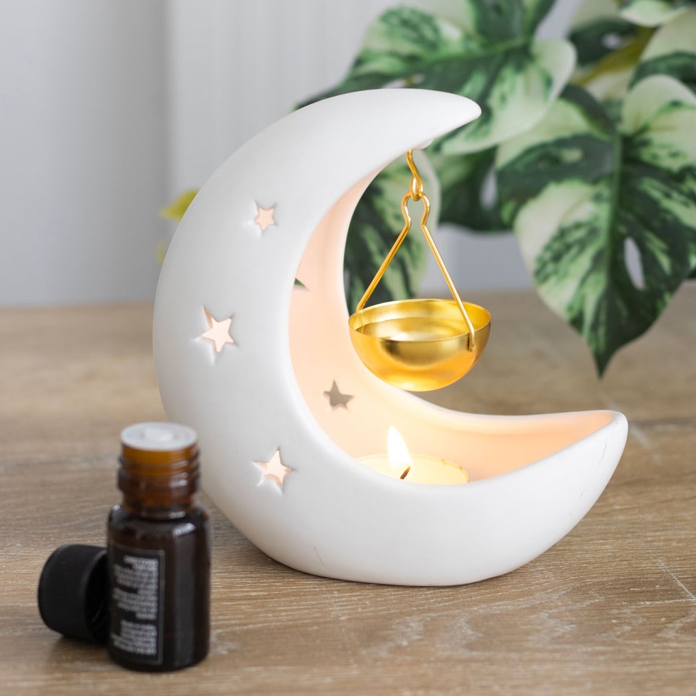 Moon-shaped oil holder with a small bottle of essential oil on a wooden surface.