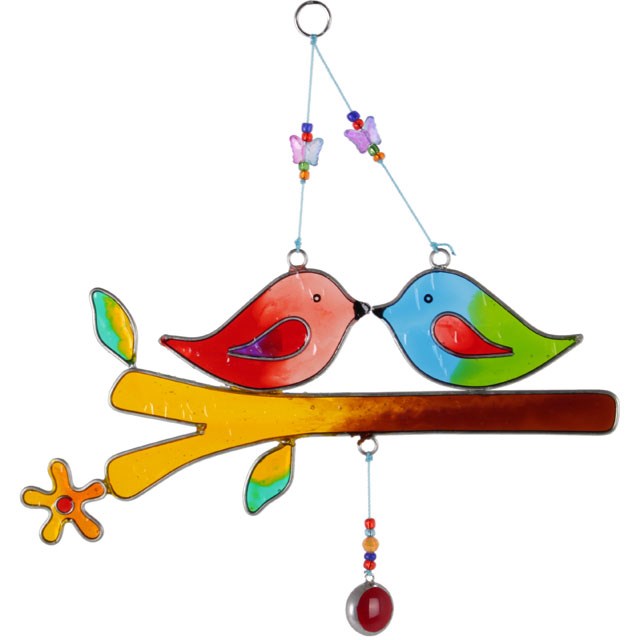 Suncatcher featuring two kissing love birds on a branch. One bird is made from glass with shades of red and the other is made form glass with shades of blue and green and a red wing. Features a coloured droplet at the bottom in red. 