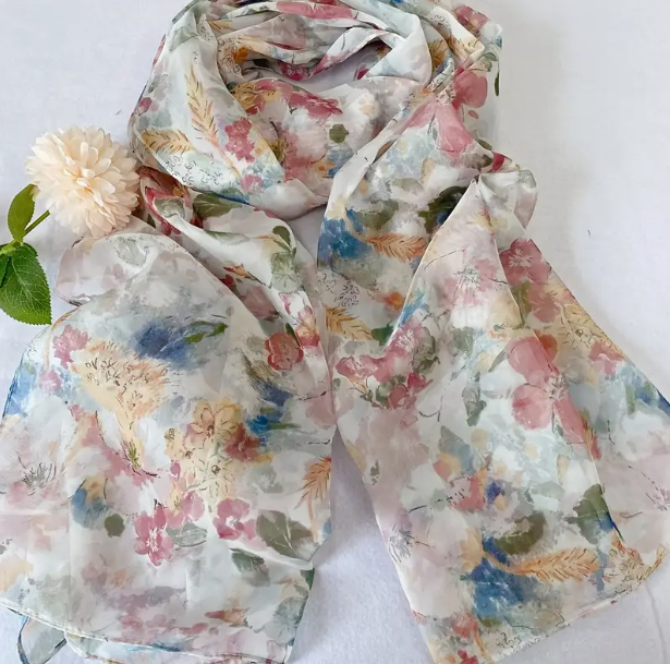 Scarf with white background and detailed floral design with pink, yellow, blue flowers, and a touch of green with some leaves. 