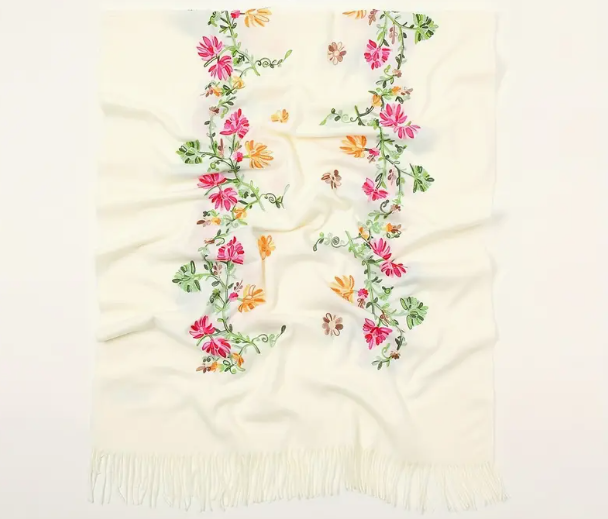 White shawl with fringe at the edge. Embroidered with a floral design featuring green vine and pink and orange flowers. 