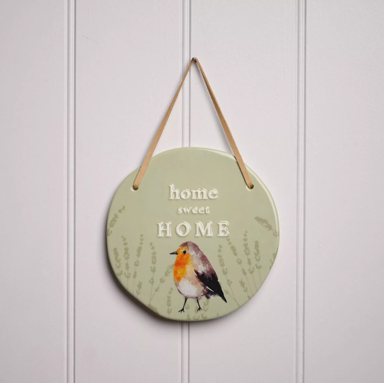 Green circle hanging plaque with darker green monochrome reeds on the bottom half on the plaque and a colourful robin over them. Above the robin is the quote 'home sweet home' and a serif font.