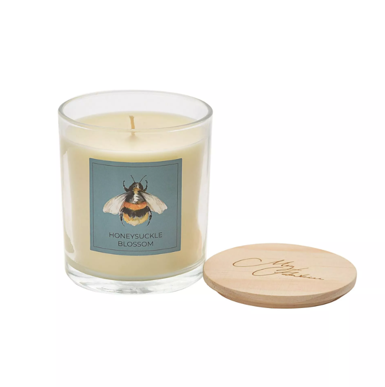White candle in clear glass jar with watercolour bee design on a square teal label on the front. Features wooden lid with 'meg hawkins' engraved in a  script font.