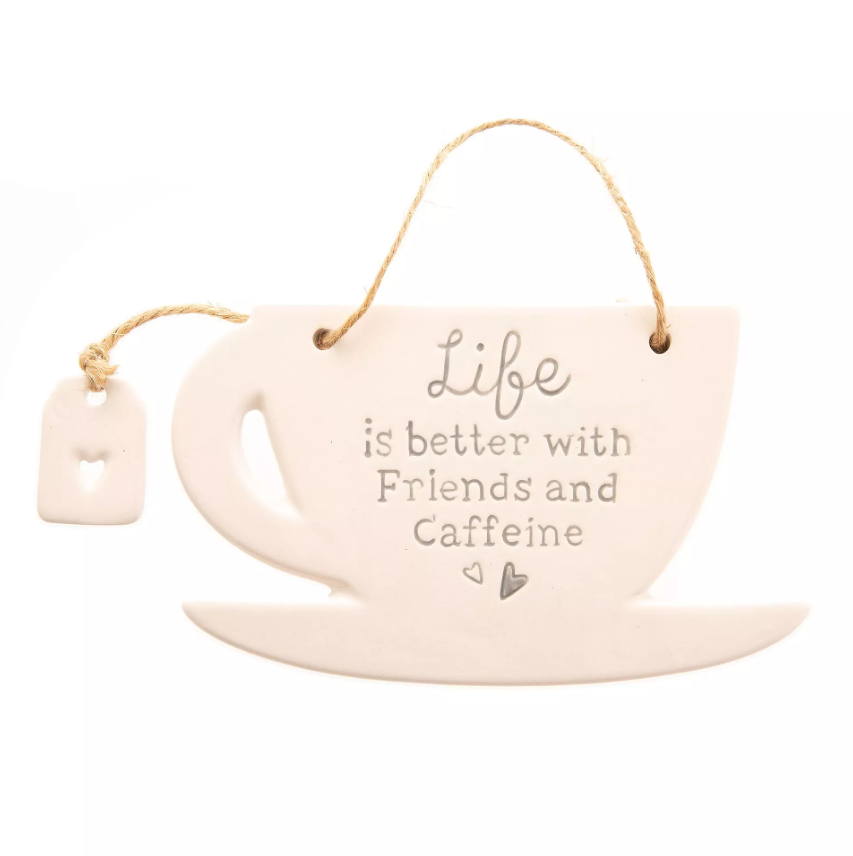 Cream ceramic hanging decoration in the shape of a mug on a coaster with the quote 'Life is better with friends and caffeine' printed on the front. Features a little ceramic teabag charm with a heart cutout, attached to the mug by twine. 