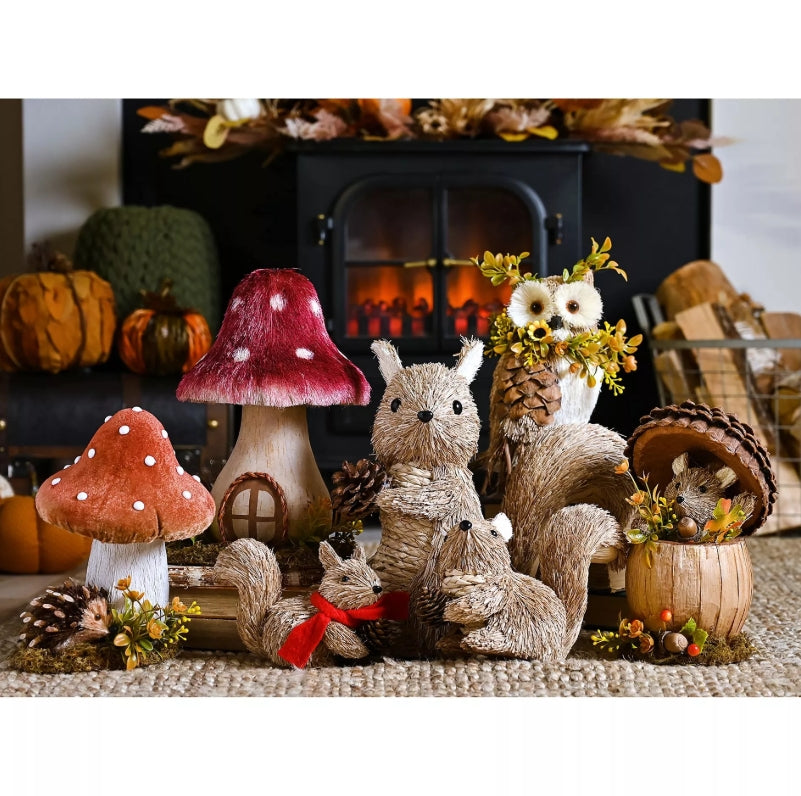 Decorative autumn scene with plush animals, mushrooms, and pinecones in front of a fireplace.