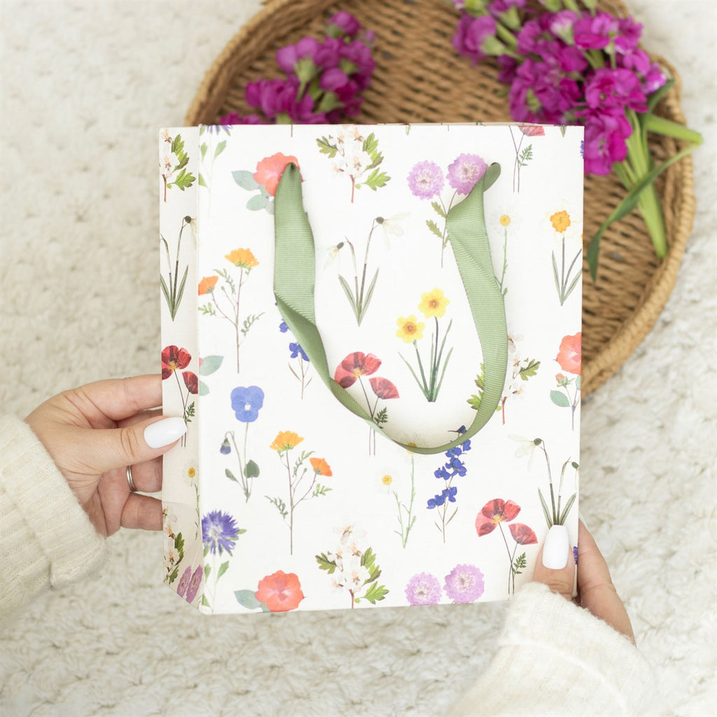 White paper gift bag featuring a floral design and green ribbon handles.