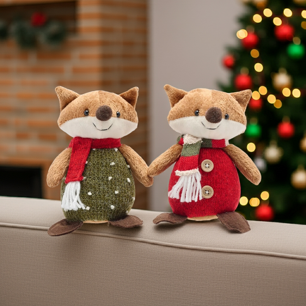 Two plush fox toys holding hands on a surface with a Christmas tree in the background.